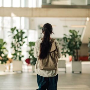 Jeune étudiante marchant dans un bâtiment universitaire ou collégial moderne, portant un sac à dos, représentant l'éducation et les nouveaux débuts.