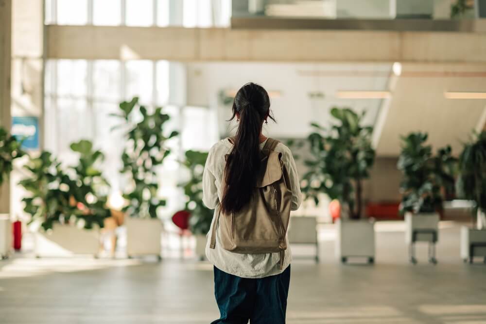 Jeune étudiante marchant dans un bâtiment universitaire ou collégial moderne, portant un sac à dos, représentant l'éducation et les nouveaux débuts.