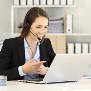Un téléopérateur souriant échange en visioconférence avec des clients depuis le bureau.