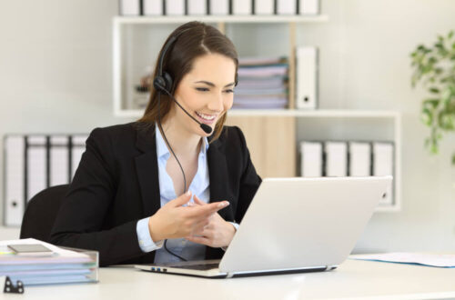Un téléopérateur souriant échange en visioconférence avec des clients depuis le bureau.